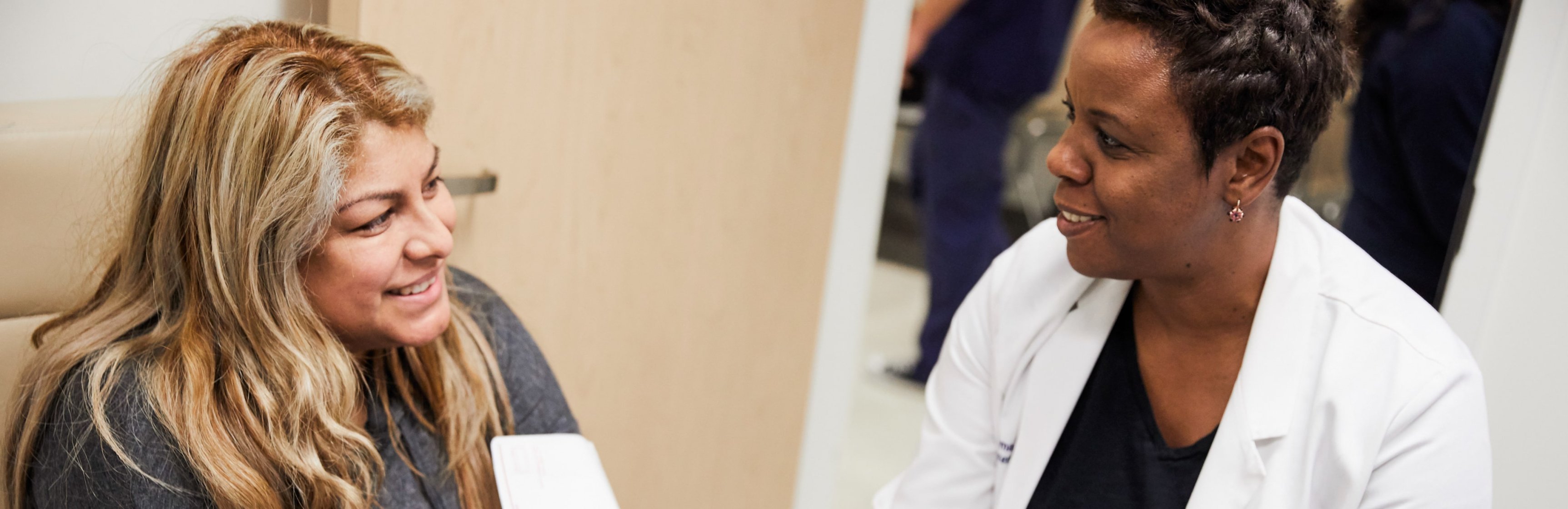 Paciente mujer latina sonriendo a una médica de color con bata blanca