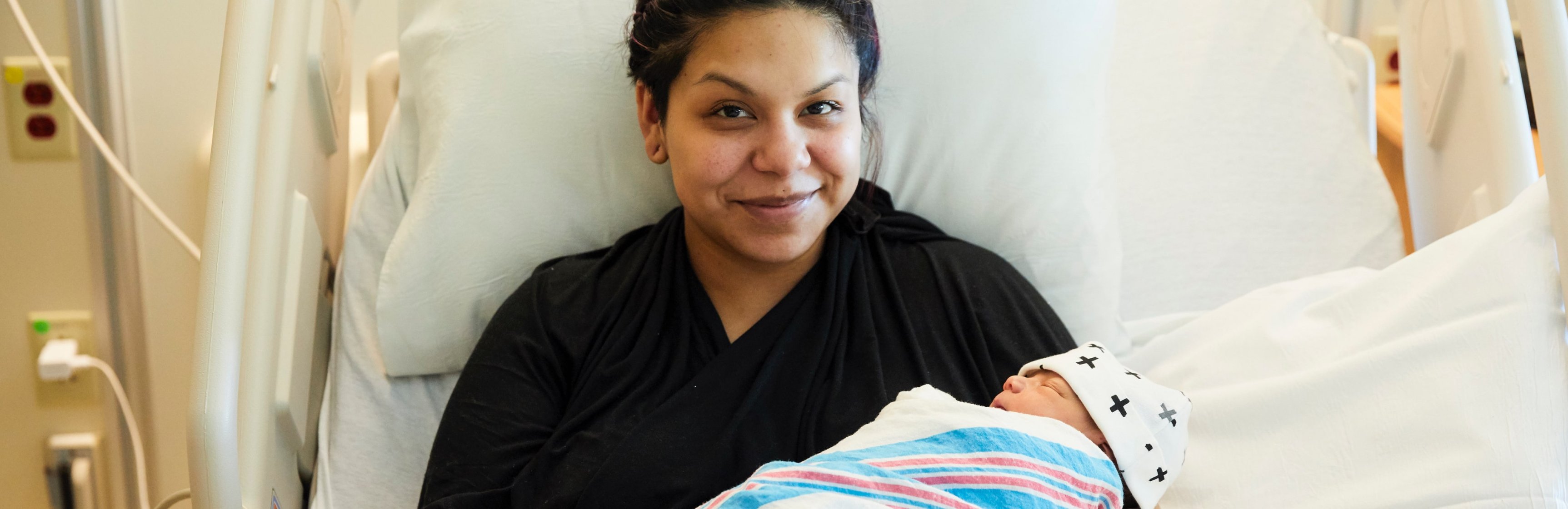 Mamá latina sonriente en una cama del hospital sostiene a su bebé recién nacido