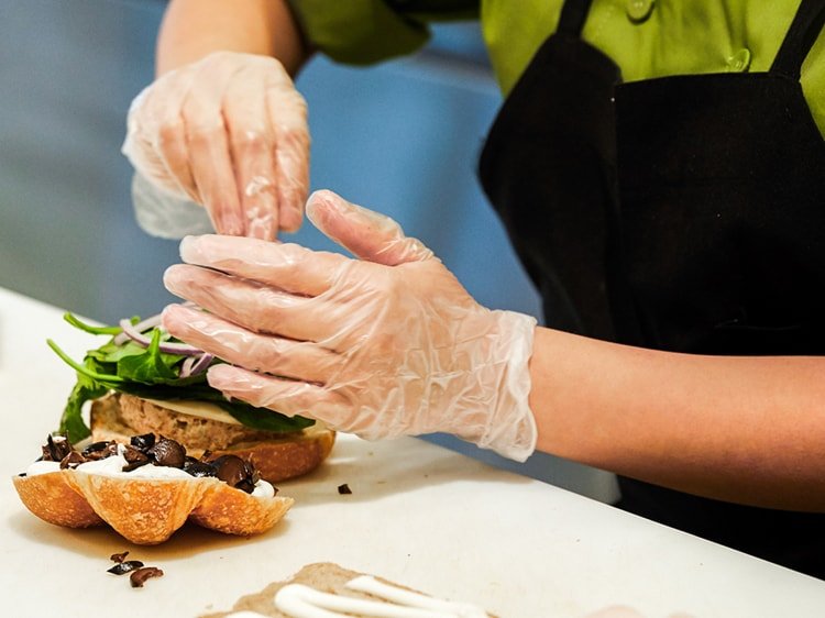 Primer plano de manos con guantes preparando un sándwich
